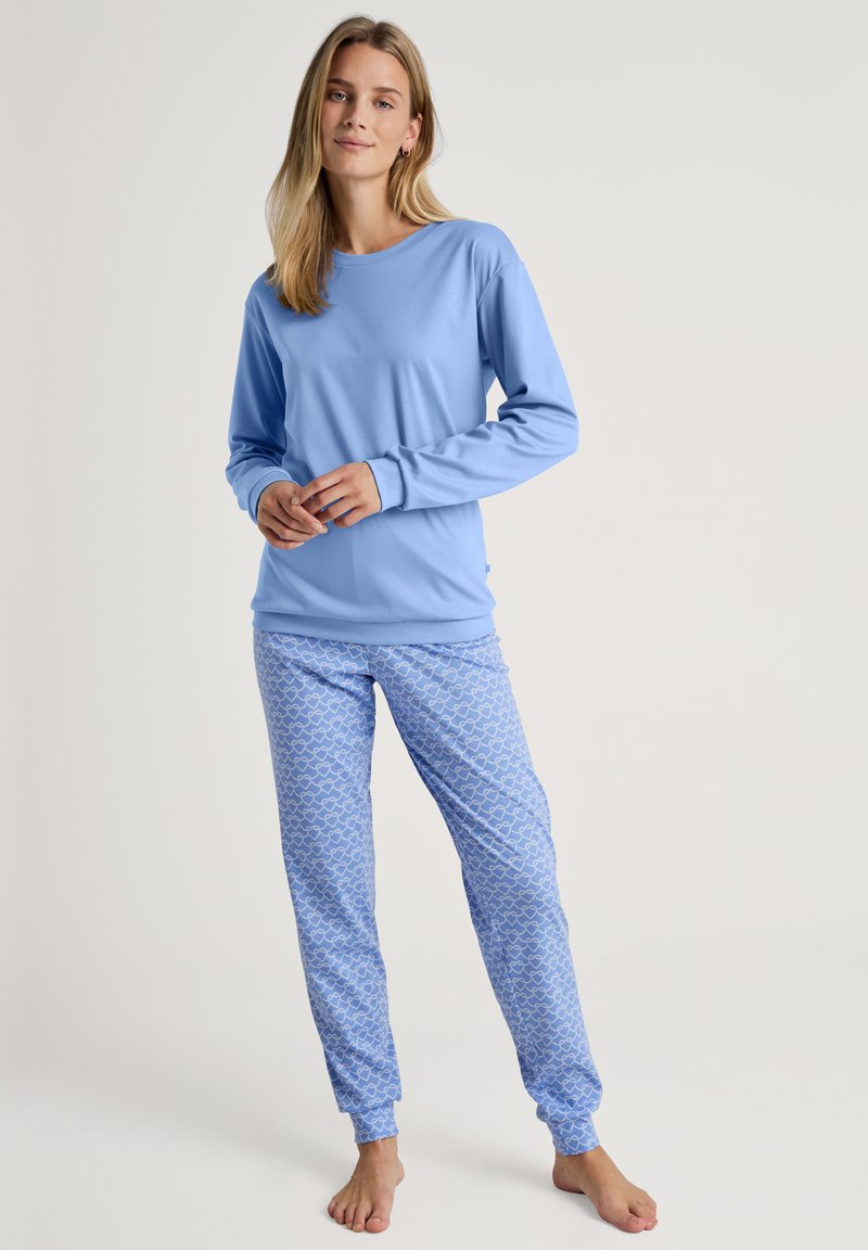Helles, blaues langärmliges Oberteil kombiniert mit passenden, hellblauen Schlafanzughosen mit einem Muster aus kleinen weißen Herzen. Weicher Stoff, lockere Passform.