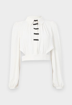 Hvid kort bluse med krave, lange puffærmer og en knaplukning prydet med sorte bånddetaljer. Glat stofstruktur.
