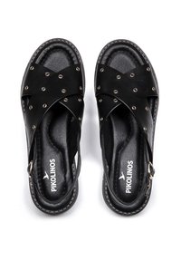 Sandalias de cuero negro con tiras cruzadas, acentos de tachuelas plateadas, talón abierto y hebilla ajustable. Textura suave con plantilla acolchada.