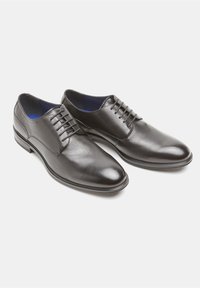 Scarpe stringate in pelle nera con finitura liscia, punta affusolata e interno blu. Presentano un design minimalista e una silhouette slanciata.