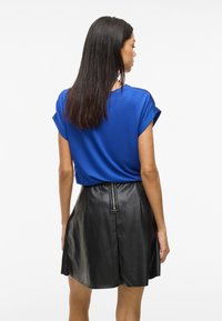 Top blu corto a maniche corte abbinato a una gonna in pelle nera con chiusura a zip sul retro, che enfatizza le texture lisce e i colori a contrasto.