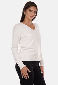Maglione bianco a scollo a V con polsini e orlo ribattuti. Tessuto morbido, vestibilità rilassata e maniche lunghe. Abbinato a pantaloni neri aderenti.