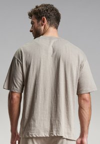 Beige, rövid ujjú póló, laza szabással, puha, strukturált anyagból készült, kerek nyakkivágással és látható varrási részletekkel a háton.