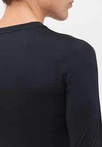 Detailopname van de bovenrug en schouder van een persoon die een strak-gezette zwarte langetermijn-shirt draagt met zichtbare naaddetails.