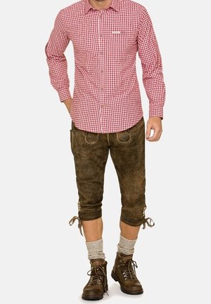 Homme portant une chemise à carreaux rouge et blanc, un lederhosen en cuir brun longueur genou avec broderies, des chaussettes beige et des bottes de randonnée marron.