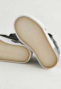 Scarpe basse bianco e nero con suola in gomma testurizzata caratterizzata da un motivo a spina di pesce e bordi arrotondati per una maggiore aderenza.