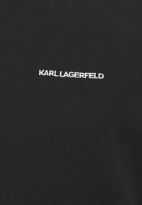 Maglietta nera in cotone con testo ricamato bianco che recita "KARL LAGERFELD" sul petto. Texture liscia, design classico con colletto tondo.