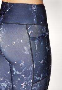 Mörkblå leggings med abstrakta vita mönster, tillverkade av stretchmaterial. Har hög midja och en sidoficka för förvaring.