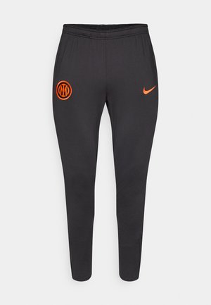 Black sweatpants with an elastic waistband, tapered design, orange Nike logo, and orange circular emblem on the thigh. Soft, smooth fabric.