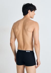 Schwarze Boxershorts mit einer enganliegenden Passform und einem elastischen Bund, der mit dem weißen "BOSS"-Logo versehen ist. Glatte Stofftextur.