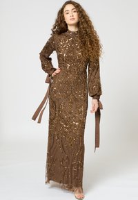 Bruine avondjurk met intricat gouden kralen, lange mouwen met strikken en een getailleerd silhouet met een vloeiende rok. Glanzende textuur.