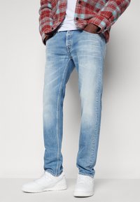 Jeans de mezclilla de color azul claro con un corte recto, que presentan una textura desgastada y un diseño tradicional de cinco bolsillos, complementados con zapatillas blancas.