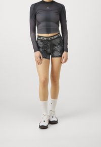 Musta pitkähihainen urheilupaita, jossa on harmaa pistekuvio, yhdistetty mustiin ja harmaisiin käärmeennahkakuosisiiin shortseihin, valkoisiin sukkiin ja urheilukenkiin.