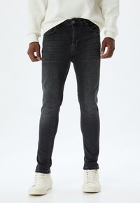 Vaqueros gris oscuro de corte ajustado, hechos de mezclilla, con bolsillos frontales, cremallera y un ligero desvanecimiento. Combinados con deportivas blancas.