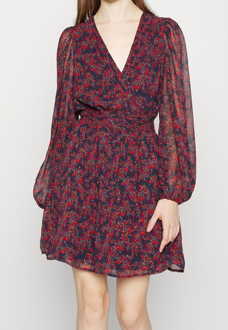 Robe courte à fleurs en tissu léger et transparent. Fond bleu foncé avec un motif floral rouge et vert. Présente un décolleté en V et des manches bouffantes.