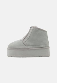 Bottine en daim gris avec une semelle épaisse et une couture ton sur ton, présentant un design sans couture et une fermeture éclair à l'avant pour un enfilage facile.