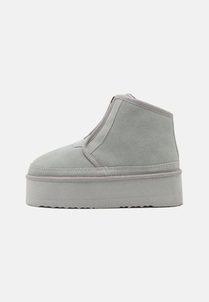 Bottine en daim gris avec une semelle épaisse et une couture ton sur ton, présentant un design sans couture et une fermeture éclair à l'avant pour un enfilage facile.