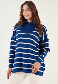 Sinine triibuline pullover, mis on valmistatud pehmest kudumkangast. Omab pool-äkkedega kaela, pikki varrukaid ning lõdva lõikega ribadega detailideks.
