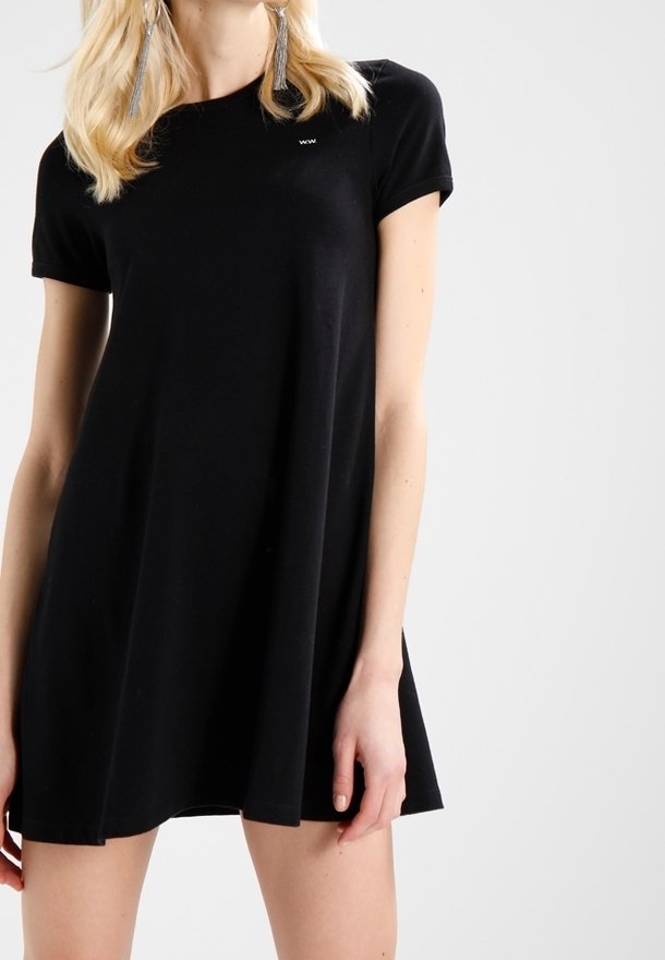 Černé krátké šaty s volným střihem, vyrobené z měkké látky. Mají malé logo na hrudi a sahají těsně nad kolena.