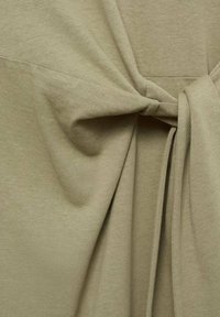 Khaki kangaskangas, jossa on solmittu yksityiskohta, pehmeä rakenne ja virtaavat laskokset, jotka esittelevät yksinkertaisia linjoja ja puhdasta, rentoa muotoilua.