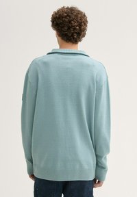 Hellblauer Strickpullover mit Schalkragen, gerippten Bündchen und Saum sowie einer lässigen Passform. Der Stoff wirkt weich und strukturiert.