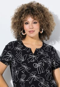Top negro con estampados de lazos blancos, mangas cortas y escote en V. La tela parece suave con una textura ligera.