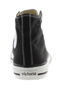 Baskets montantes en toile noire avec coutures blanches, écusson rond, et semelle en caoutchouc blanche, présentant un design épuré.