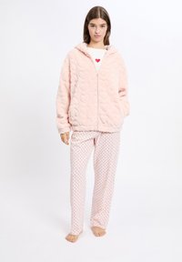 Różowa, puszysta kurtka zapinana na zamek z wzorem serc, w połączeniu z kremowymi spodniami w czerwone grochy. Miękka faktura, luźny krój, z kapturem.