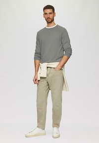 Felpa grigia chiara con colletto bianco, pantaloni beige e sneakers bianche. La felpa è annodata in vita con un indumento in maglia di colore chiaro.