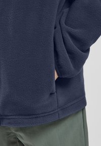 Tume meresinine fliisist pullover, pehme tekstuuriga, lõdva lõikega ja küljetaskutega. Helmedel on diskreetne õmblusdetail.