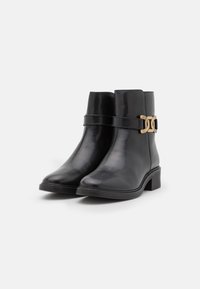 Bottes noires en cuir avec une finition lisse, dotées d'un talon plat, d'une sangle et d'une boucle dorée sur le côté.