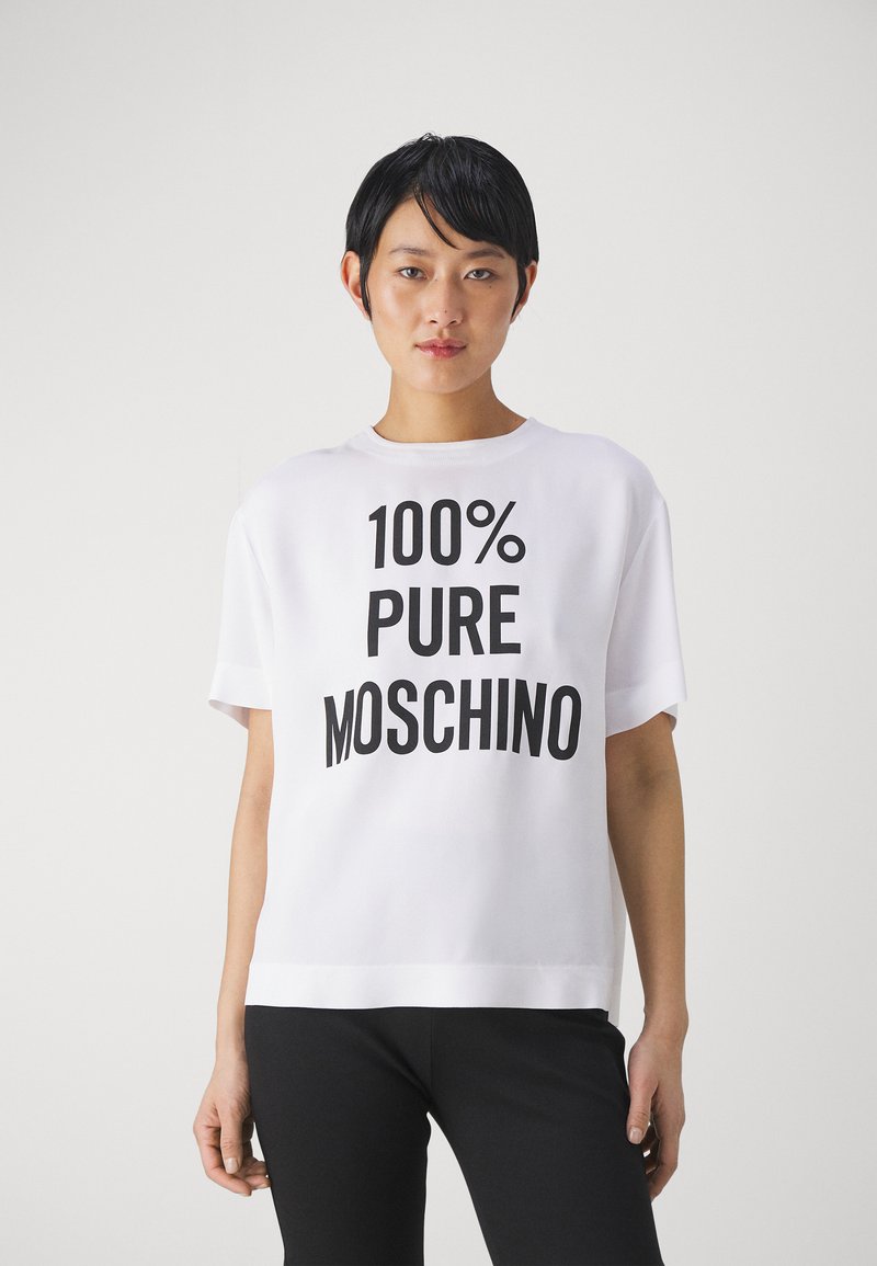 Balta trumpa rankovėmis marškinėliai su laisvu kirpimu, ant kurių priekio ryškiu juodu tekstu parašyta "100% PURE MOSCHINO". Lygus audinys, minimalistinis dizainas.