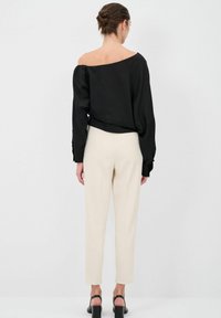 Blusa nera off-the-shoulder con maniche lunghe, abbinata a pantaloni tapered crema e sandali neri con tacco bloccato. Tessuto morbido, vestibilità rilassata.