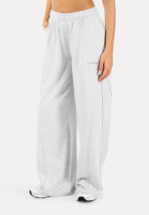 Persoon draagt wijde lichtgrijze joggingbroek met elastische taille en witte sneakers, staand met handen in de zakken.