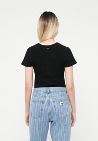 Haut noir texturé à manches courtes avec un col rond, associé à un jean à rayures verticales bleu clair avec un patch logo sur la poche arrière.