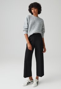 Lichtgrijze, fuzzy-textuur trui met een ronde hals, gecombineerd met hoge taille, zwarte losse broek en witte sneakers met zwarte accenten.