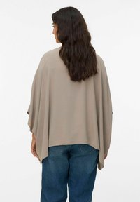 Taupe värvi lahti sobiv kimono-stiilis särk, mis on valmistatud kergest kangast, omab langevaid varrukaid ja sirget äärt, kombineeritud siniste teksadega.