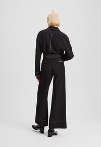 Black long-sleeve shirt with white stitching and a collar, paired with wide-leg black pants featuring stitched accents and a back logo.