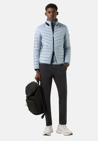 Light blue puffer jacket with chevron pattern, black accents. Dark pants, white sneakers, and a black backpack with top flap.