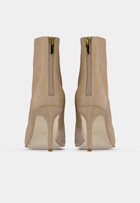 Cizme scurte bej cu toc înalt, din piele intoarsă fină, cu fermoare la spate și toc subțire tip stiletto. Au vârf rotund și accente texturate.