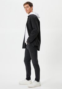 Musta farkkutakki valkoisen hupparin päällä, mustat slim-fit-farkut ja valkoiset lenkkarit, joissa on rento istuvuus ja selkeä muotoilu.