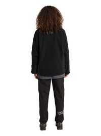 Person med krøllet hår står med ryggen til, iført en sort jakke, sorte bukser med "223" på venstre ben og sorte sko.