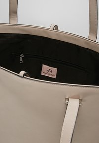 Beige tote taske lavet af glat syntetisk materiale, med dobbelt skulderremme, åben top og sort indre med en lynlås lomme. Etikette synlig indeni.