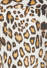 Tessuto con stampa leopardata caratterizzato da macchie irregolari in tonalità di marrone e nero su uno sfondo color crema, con texture e dimensioni dei pattern variabili.