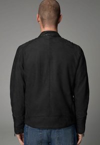 Chaqueta de cuero negra con una textura suave, acentos acanalados en los hombros y un diseño limpio. Detalles de cremallera en las mangas y una forma ajustada.
