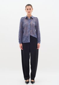 Bluză din dantelă de culoare albastru deschis, cu modele florale intricate. Mâneci lungi, guler cu nasturi, combinată cu pantaloni negri largi și pantofi fără toc.