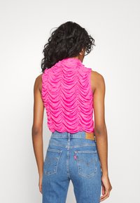 Top sem mangas fúcsia com design texturizado franzido, combinado com jeans de denim azul de cintura alta com bolsos traseiros clássicos e costura.