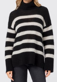 Pull à col roulé rayé noir et blanc en matière douce et duveteuse. Coupe ample avec manches longues et ourlet côtelé.