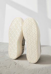 Baskets avec une tige en tissu à motifs gris et blanc ; semelles en caoutchouc blanches avec un motif de grip texturé et impression de logo.