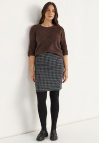 Brauner, flauschiger Pullover, grauer Karomuster-Bleistiftrock, schwarze Leggings und schwarze Slipper. Das Outfit hat eine weiche Textur mit einer figurbetonten Silhouette.